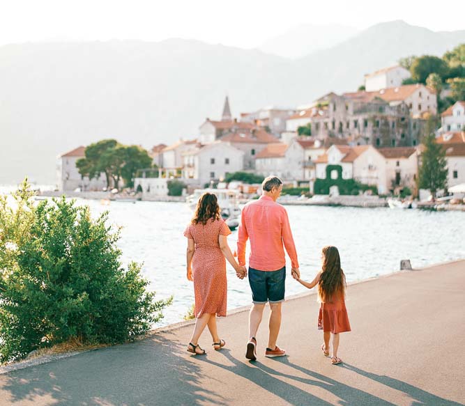 mom dad little girl walk holding hands along perast embankment montenegro back view